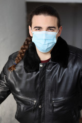 Young attractive guy with long hair wearing a protective medical mask and gloves due to Corona virus. Safety, protection, Covid-19 concept.