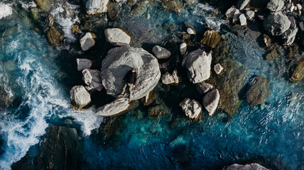 Fototapeta na wymiar Aerial shot above a man lay down on the rock in blue river New Zealand.