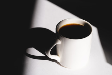 cup of coffee on white background. Cup of fresh hot espresso. sun rays in daylight, hard light and shadows concept.