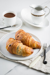 Breakfast with coffee and croissant in white cup and plate on marble background. Healthy homemade pastry, copy space