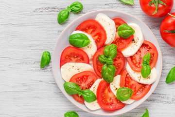 Caprese salad with ripe tomatoes and mozzarella cheese with fresh basil leaves in a plate. top view