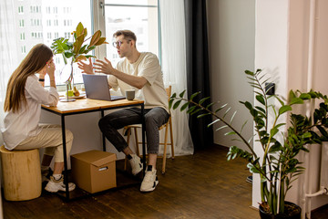 young caucasian woman prevents her husband from working at home, man sit with laptop and yelling at...