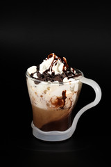 Hot chocolate or coffee beverage in glass cup with holder, isolated on black. Visible coconut crumbs, milk, whipped cream and other sweet ingredients.