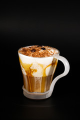Hot chocolate or coffee beverage in glass cup with holder, isolated on black. Visible coconut crumbs, milk, whipped cream and other sweet ingredients. Caramel