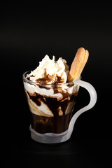 Hot chocolate or coffee beverage in glass cup with holder, isolated on black. Visible coconut crumbs, milk, whipped cream and other sweet ingredients and holip