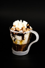 Hot chocolate or coffee beverage in glass cup with holder, isolated on black. Visible coconut crumbs, milk, whipped cream and other sweet ingredients and peanuts