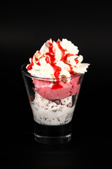 Hot chocolate or coffee beverage in glass cup with holder, isolated on black. Visible coconut crumbs, milk, whipped cream and other sweet ingredients and icecream