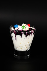 Hot chocolate or coffee beverage in glass cup with holder, isolated on black. Visible coconut crumbs, milk, whipped cream and other sweet ingredients and candy