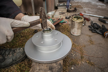 Hammering new bearing shell or race into car hub and brake disc using a hammer or mallet. Home mechanic fixing wheel bearings on a car.