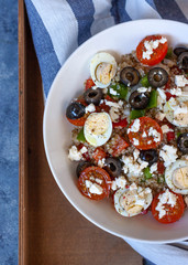 Healthy protein salad with quinoa, some vegetables and little eggs in a white bowl over a wooden tray.Top view.