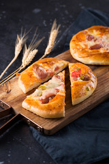 Home made small pizzas with tomatoes and cheese on wooden cutting board on dark background with wheat spikes. Healthy proper food preparation, copy space
