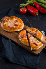 Home made small pizzas with tomatoes and cheese on wooden cutting board on dark background with wheat spikes. Healthy proper food preparation, copy space