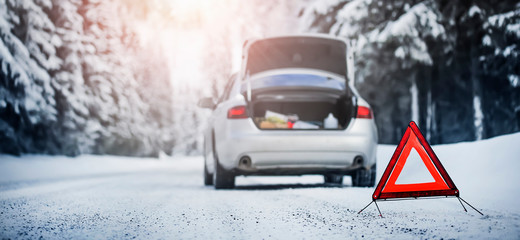 Detail of red warning triangle with a broken car on snowy road.