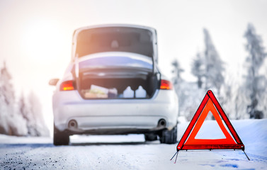 Detail of red warning triangle with a broken car on snowy road.
