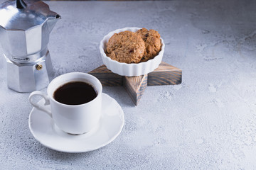 White cup of coffee with oatmeal cookies and coffee maker, breakfast concept, selective focus