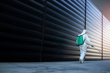 Shot of male person in white chemical protection suit doing disinfection of public areas to stop spreading highly contagious corona virus. Stop coronavirus or COVID-19. - obrazy, fototapety, plakaty