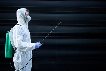 Portrait of male person in white chemical protection suit holding sprayer with disinfectant...