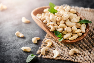 Wooden bowl with cashew nuts on dark stone table.