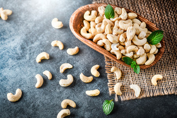 Wooden bowl with cashew nuts on dark stone table.