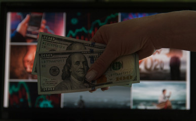 Fototapeta premium Woman holding money dollars in hand in front of the monitor with news. Crisis concept. Save money
