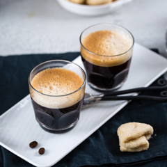 Two cups of fresh espresso on white rectangular tray with milk jar and coffee maker, copy space, breakfast concept 
