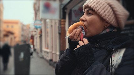 Young hungry woman traveller eats vegan meatless fast food on street at blurred European city...