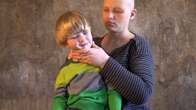 Funny fair-haired boy in colored clothes plays with attractive girl with a shaved bald head. Beautiful mother with cancer fell ill