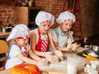 Three little chefs enjoying in the kitchen making cakes. Girls at the kitchen. Family housekeeping