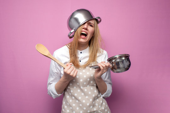 unhappy girl cook in kitchen clothes with a pan on her head cries on a colored background, woman housewife with kitchen items in stress
