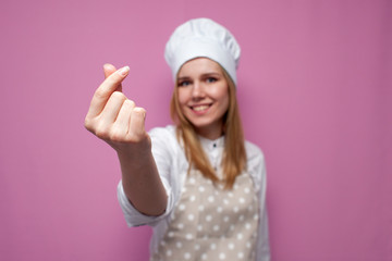 cheerful girl cook in kitchen clothes shows italian heart sign and smiles on a colored background, woman housewife makes hand gesture