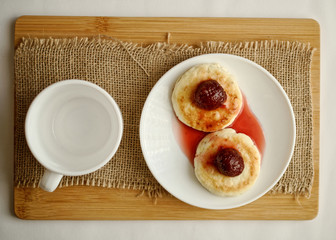 curd pancake on a white plate with strawberry jam next to a cup. top view.