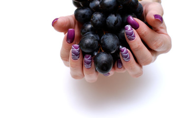 female fingers with painted nails hold a dark grape. lilac nails with a pattern.