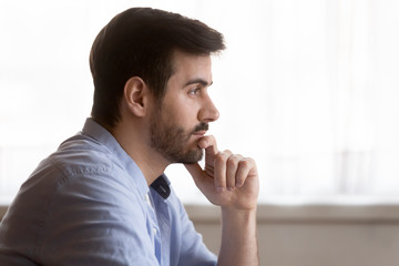 Fototapeta na wymiar Side view head shot distracted from job study young bearded man touching chin, looking away. Pensive guy planning day, thinking visualizing future, dreaming of weekend time, planning workday.