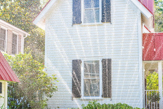 Typical American Residential House Building In Charleston, South Carolina Area With White And Red Architecture And Water Sprinklers Watering Lawn Drops Texture