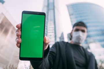 A man in a mask with a phone with a green screen in his hands