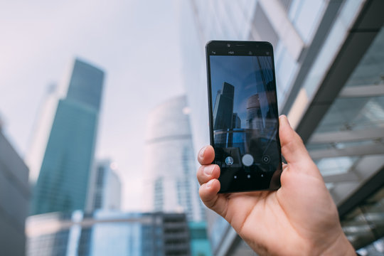 A male hand with a phone takes a picture against the backdrop of the city