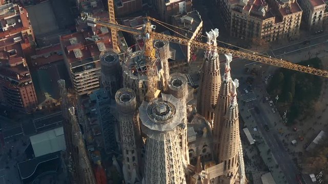 AERIAL: Close Up Overhead Circling La Sagrada Familia With Cranes In Beautiful City Sunny Haze Over Barcelona, Spain 