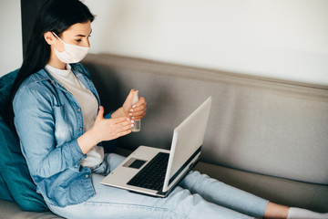 Health care and hygiene. Woman in face mask spreading sanitizer on hands before touching laptop. Infection diseases prevention