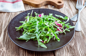 Fresh organic arugula leaves on black plate. Arugula or rucola for salad on wooden rustic background. Zero waste concept. Selective focus