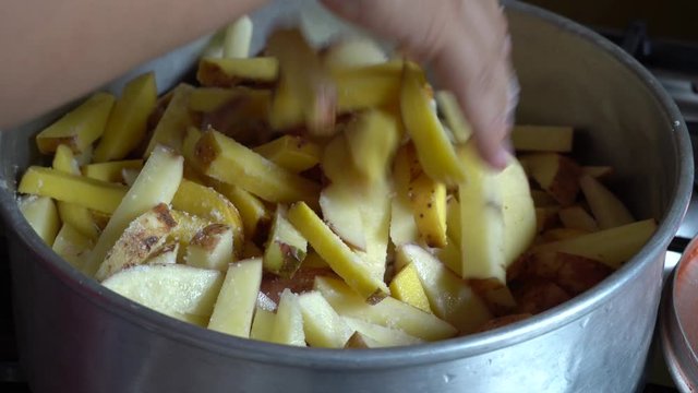the hands of a woman pouring salt on several pieces of potato and mixing