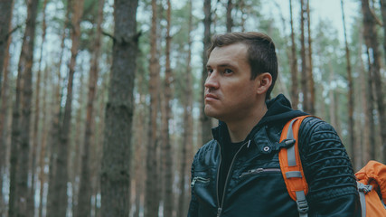 Portrait of young traveling man in woods. Close up of adult male in leather jacket with backpack in forest.