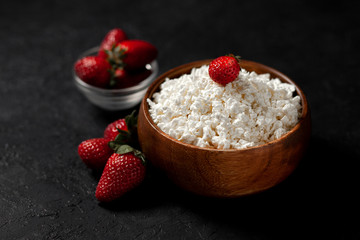 homemade fresh cottage cheese in a wooden plate without additives lies with strawberries on a black texture table