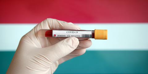 COVID-19 Pandemic Coronavirus concept ; Close-up of a Positive COVID-19 blood test sample tube with Flag of Hungary at background. Blood testing for diagnosis new Corona virus infection.