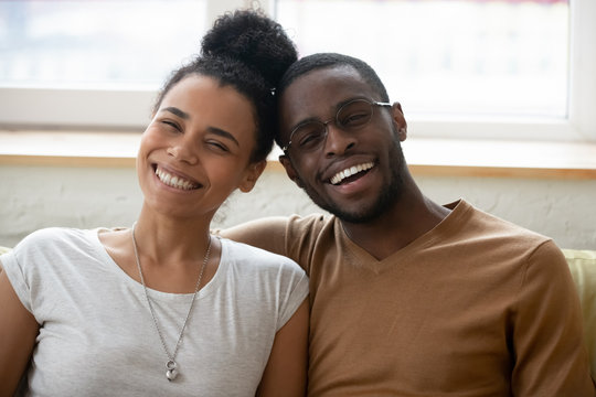 Close up portrait of young happy african american couple. Attractive smiling family of diverse woman and man looking at camera in living room at home. Husband and wife excited in love posing for photo