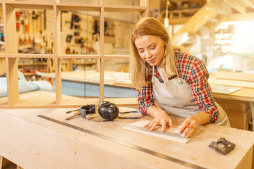 attractive caucasian carpenter lady deals with drawings during work, woman use pencil and ruler...