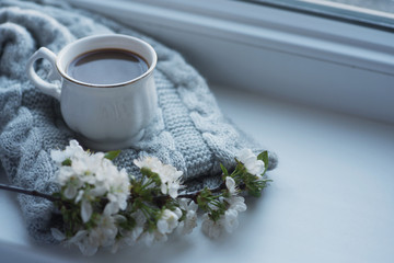The composition consists of a cup of coffee with milk, a tweed of flowers and a scarf on the window