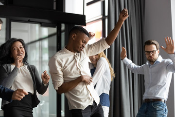 Excited happy multiracial businesspeople have fun engaged in activity in office together, overjoyed diverse colleagues dance celebrate successful business project, Friday celebration concept