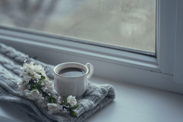 The composition consists of a cup of coffee with milk, a tweed of flowers and a scarf on the window