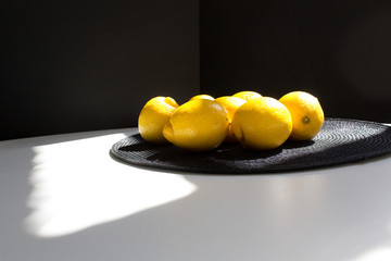 Yellow color lemons into sunny morning home kitchen on black plate  