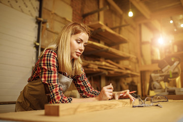 attractive professional woodworker or craftswoman during work in factory, woman deals with wooden pieces, make wooden furniture for customers